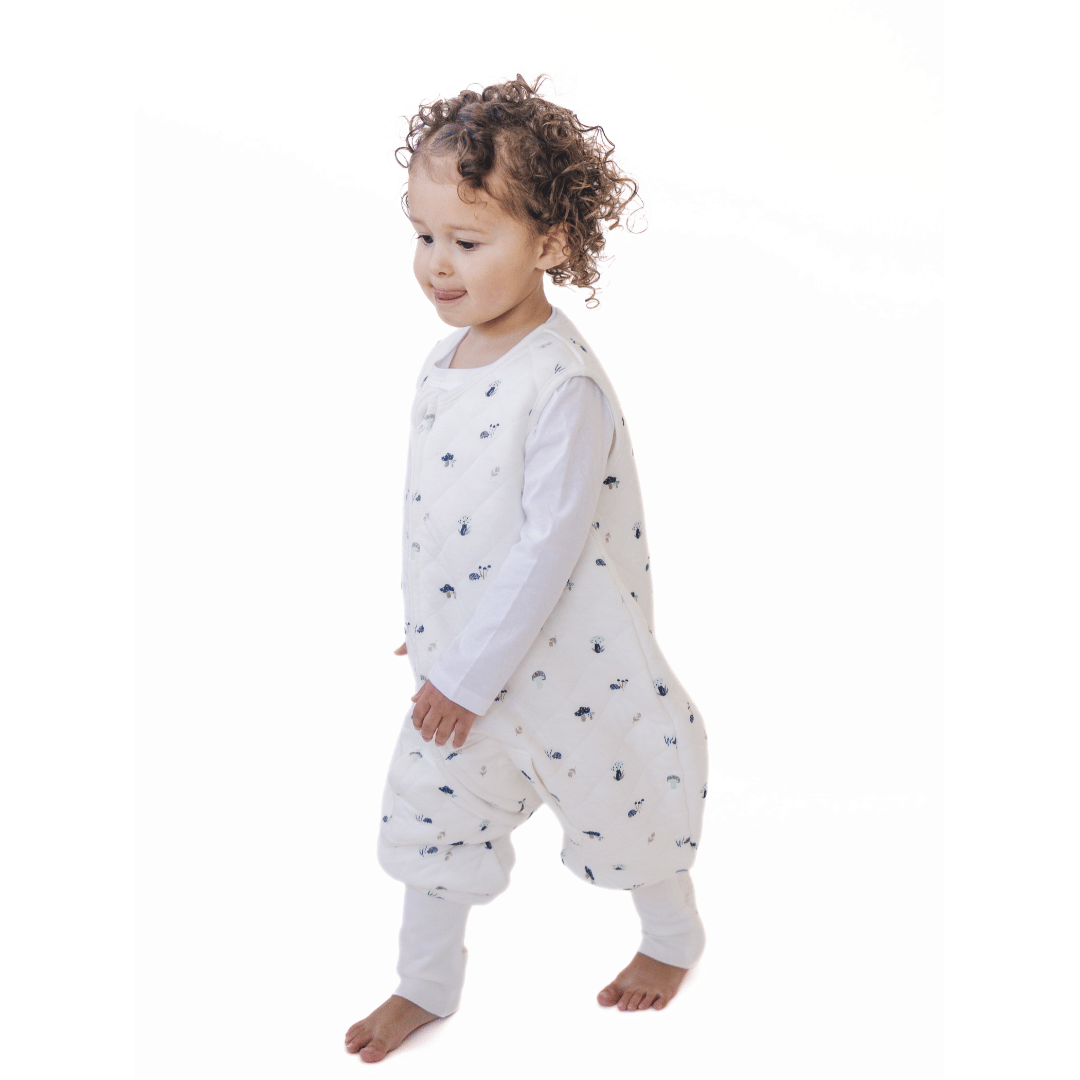 A baby standing comfortably in a Tealbee Dreamsuit, featuring buttery soft and cozy fabric made of 70% Bamboo Rayon and 30% Organic Cotton. Designed as a sleep sack with feet for walkers, ensuring both comfort and safety.