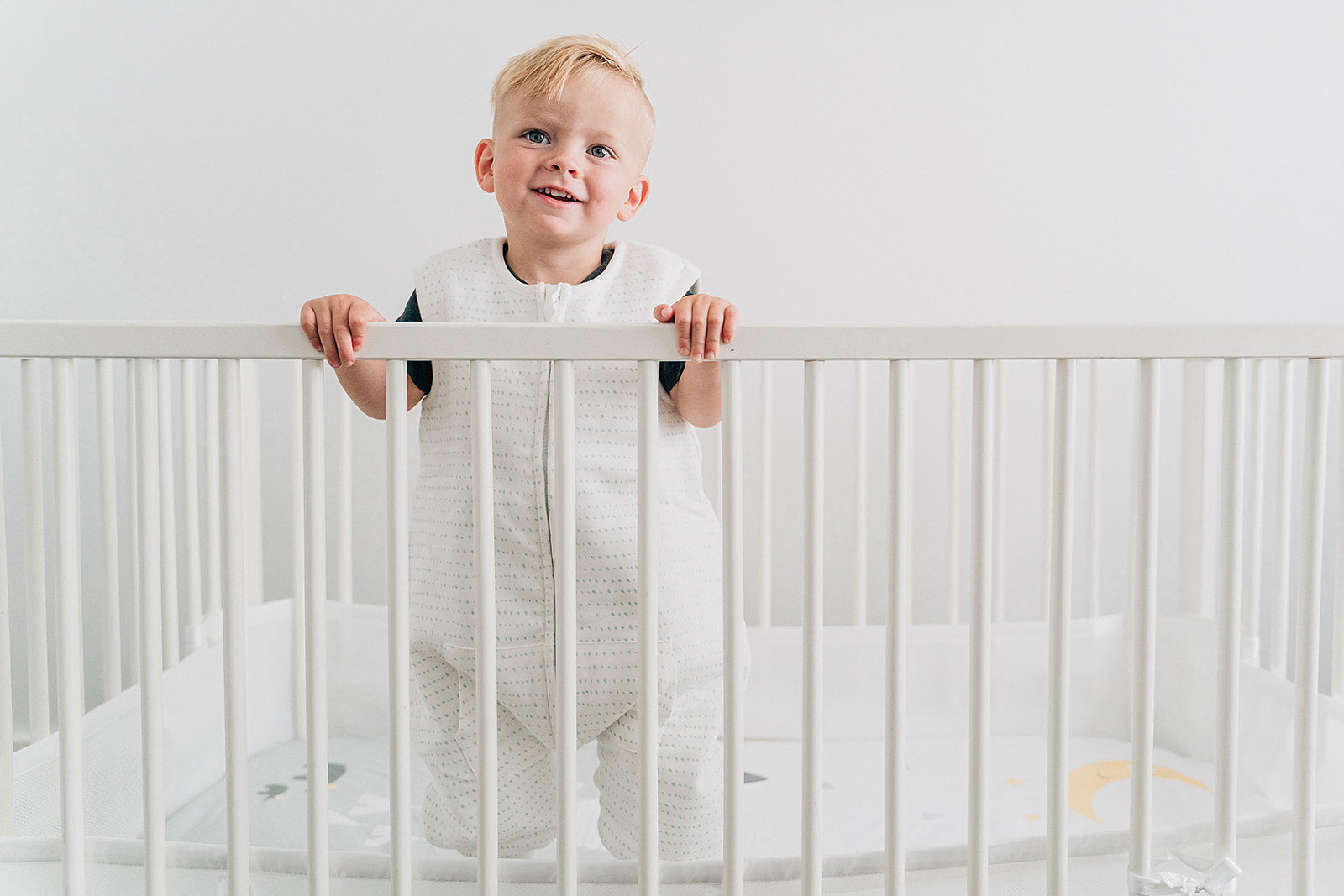 Boy wearing sleep sack with legs tealbee dreamsuit in brushed dots print in a crib