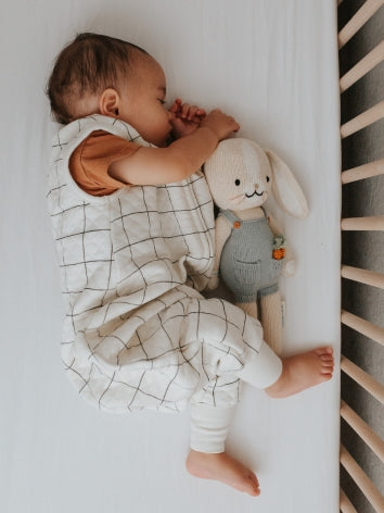 Baby sleeping on his side in a crib with Tealbee dreamsuit on