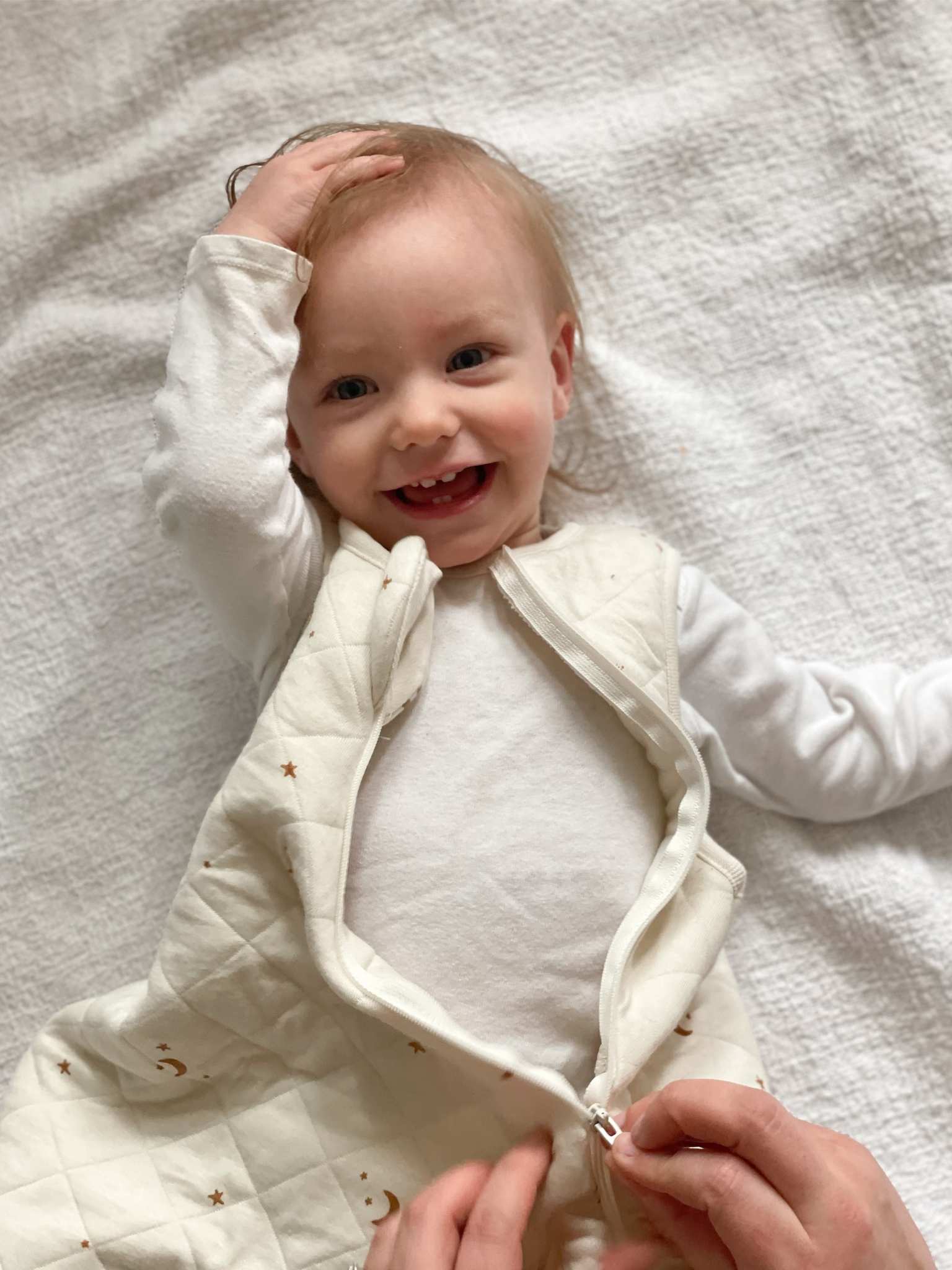 Baby lying on a white blanket wearing tealbee dreambag in moons and stars