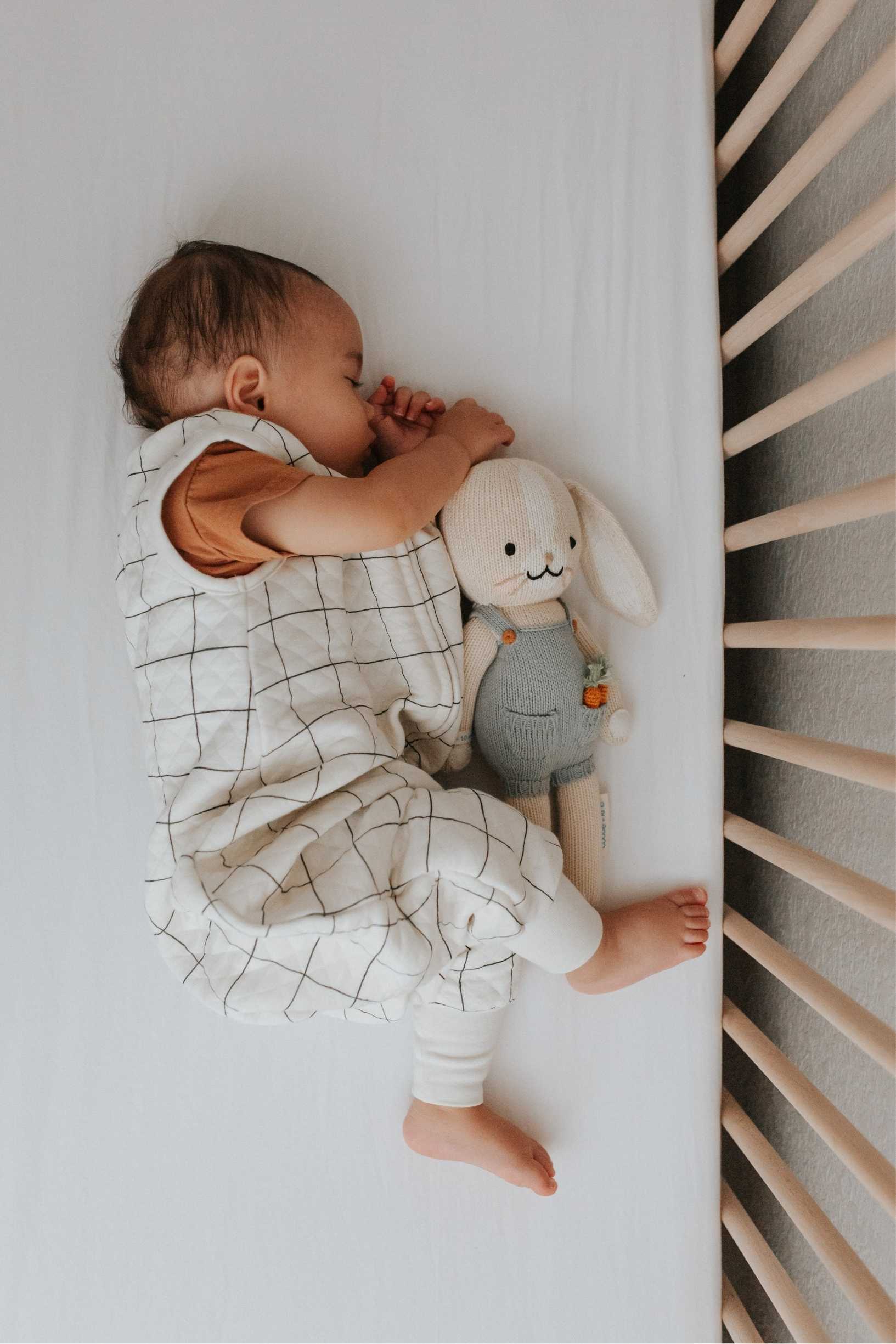 Baby sleeping in a crib wearing tealbee dreamsuit in checkered print