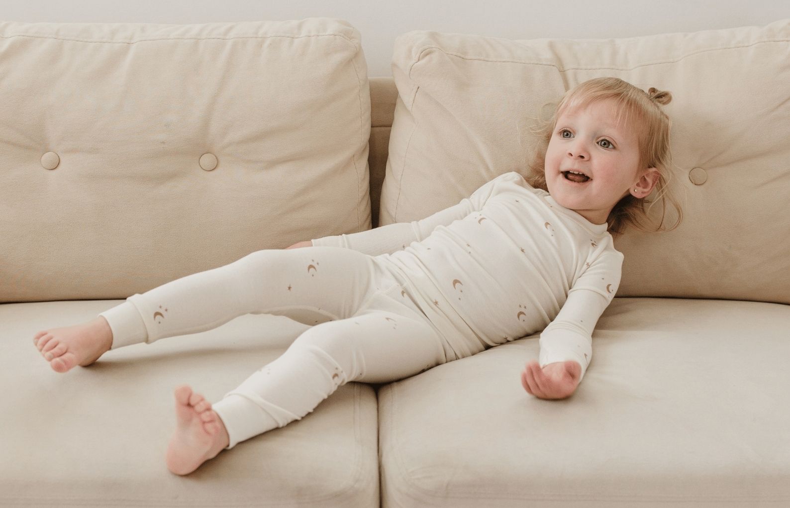 Child in tealbee pajama in moons and stars print lying on a beige couch