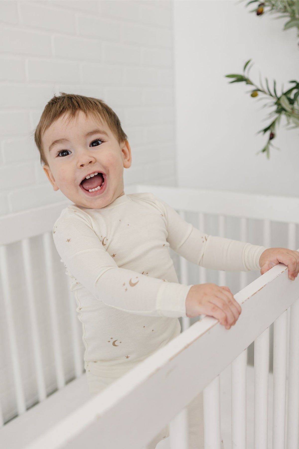 Child in a white crib wearing tealbee pajamas in moons and stars