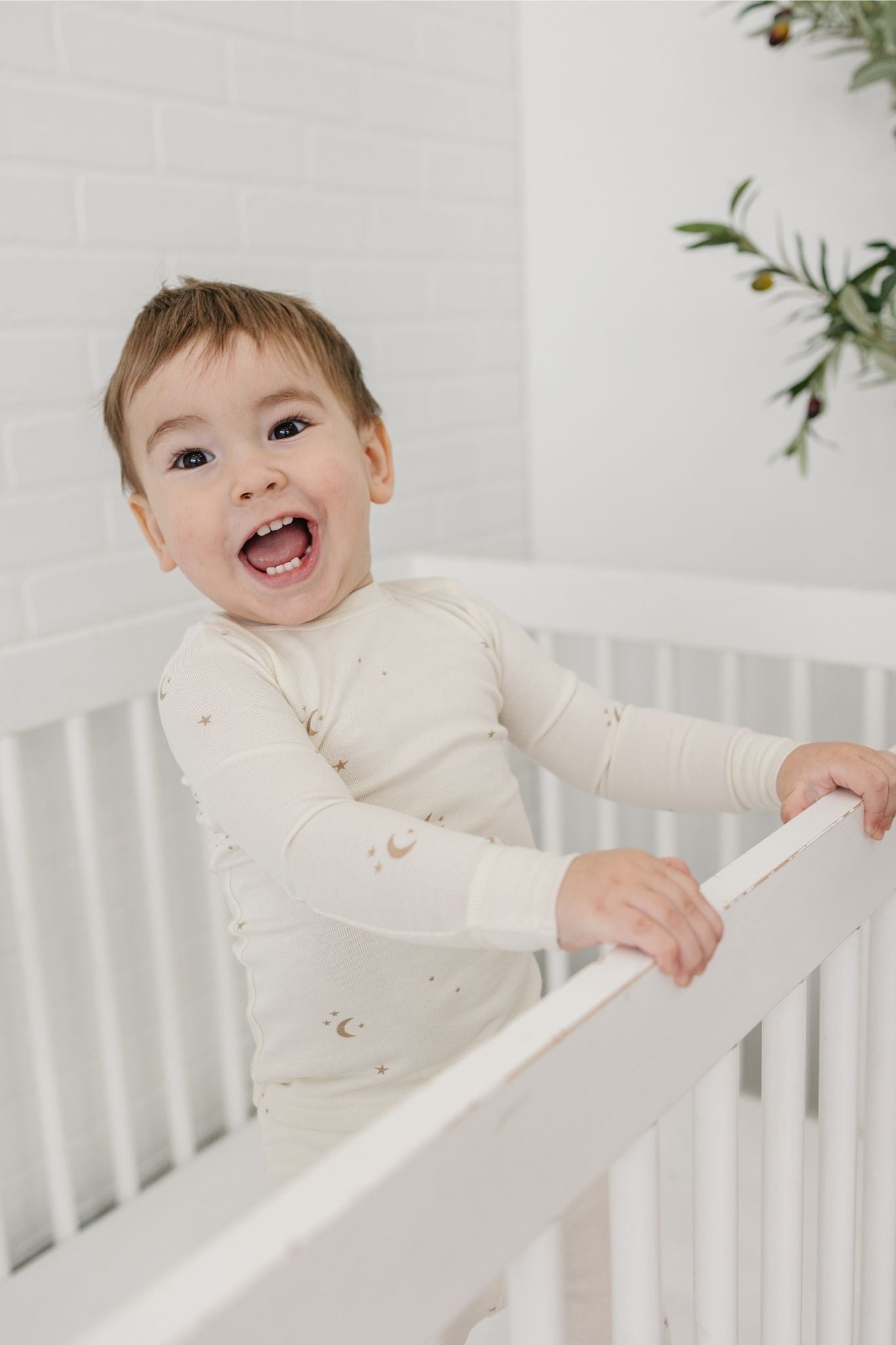 Child in a white crib wearing tealbee pajamas in moons and stars