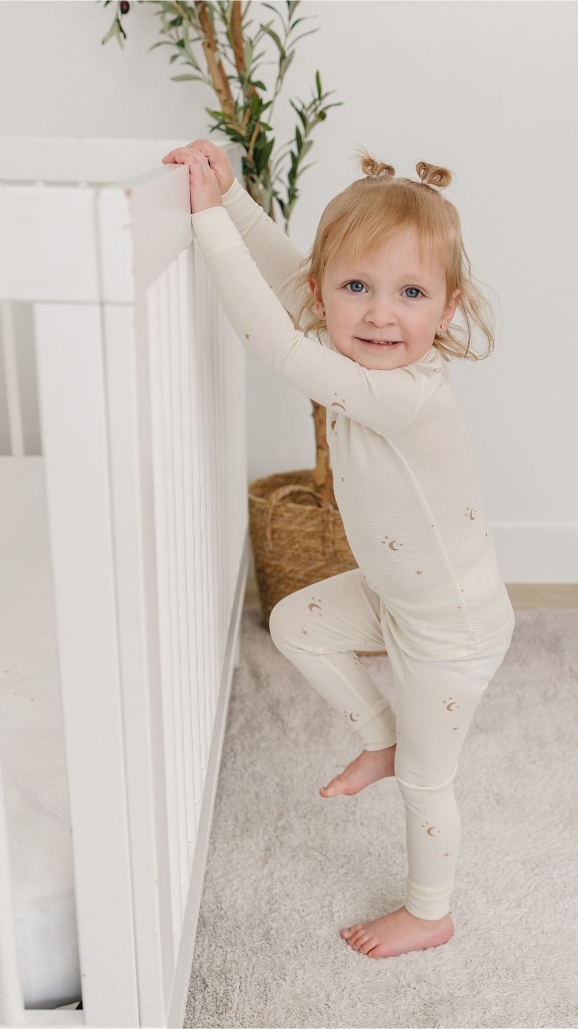 Child wearing tealbee pajamas moons and stars standing next to a crib