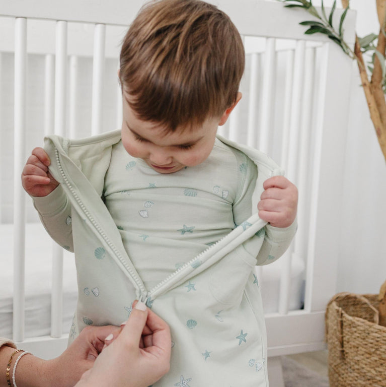 Child wearing tealbee pajamas in seashell putting on a matching tealbee dreamsuit in seashell print 