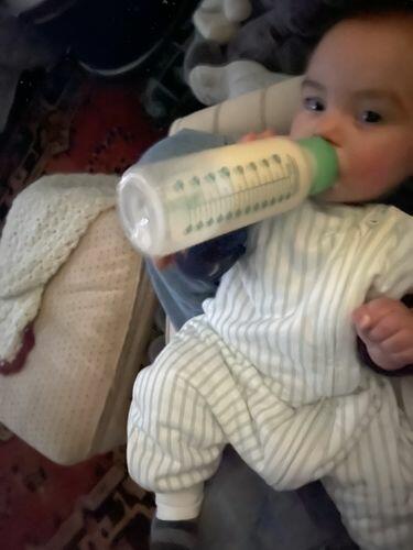 Baby in tealbee dreamsuit in minty stripes print holding a bottle 