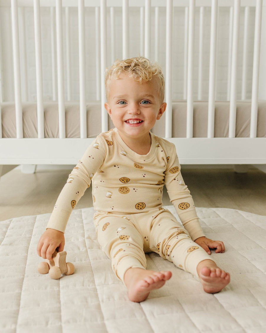 Toddler sitting by his crib in Cookies pajamas