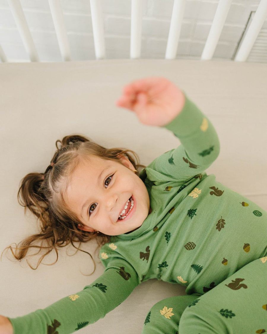 Toddler laughing on a bed in Forest pajamas