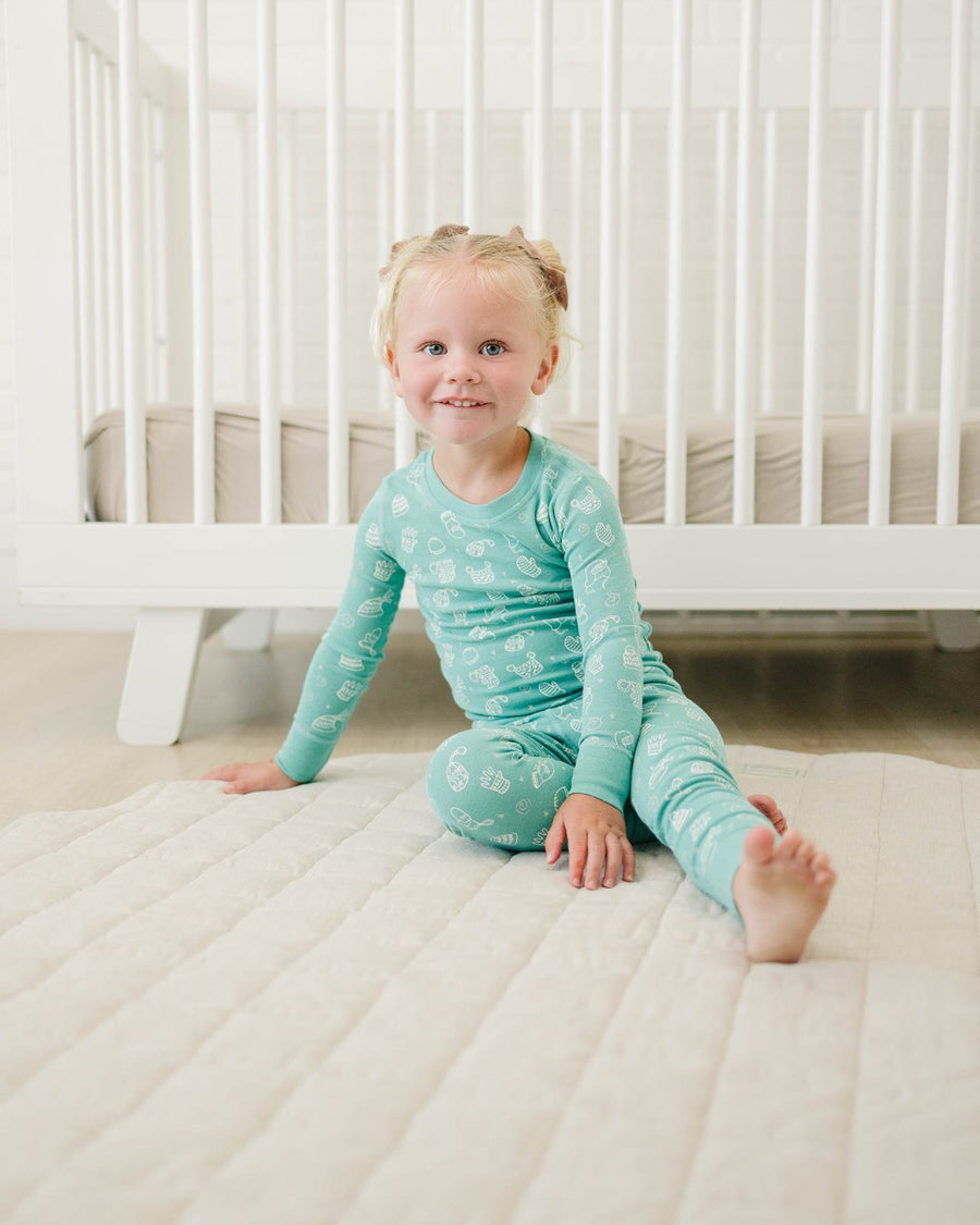 Toddler sitting on a nursery mat in Snow Day pajamas